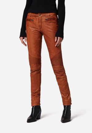Brown leather pants with a slim fit, vertical and horizontal ribbed accents, side zip pockets, and a smooth texture. Worn with black heeled boots.