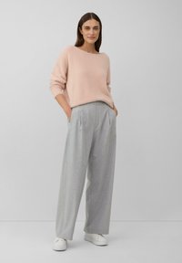 Un pull en rose clair, fluffy, avec un col large, associé à un pantalon large gris clair avec des plis et des poches, porté avec des baskets blanches.