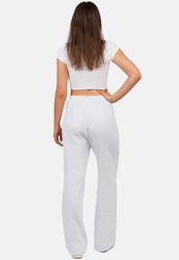 Witte, gestructureerde broek met een elastische tailleband, losse pasvorm en wijde pijpen. Het model draagt een aansluitende witte crop top, gezien van achteren.