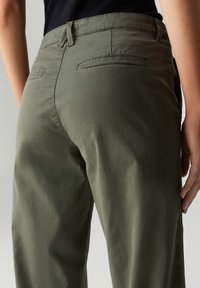 Pantaloni verde oliva con una texture liscia, dotati di tasche posteriori e una vita a media altezza, mostrati dal retro.