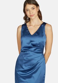 Robe en satin bleu avec un décolleté en V, sans manches, présentant des plis latéraux pour du relief et une silhouette ajustée.