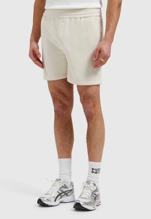 Man draagt textuurige off-white shorts, witte sportsokken met de tekst "PURE PATH" en zilverwitte hardloopschoenen, staat op een effen achtergrond.