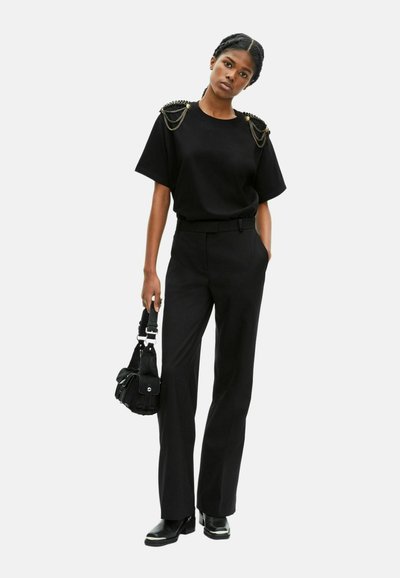 Camiseta negra de manga corta con detalles de cadena en los hombros, combinada con pantalones negros de tiro alto y un pequeño bolso negro de hombro.