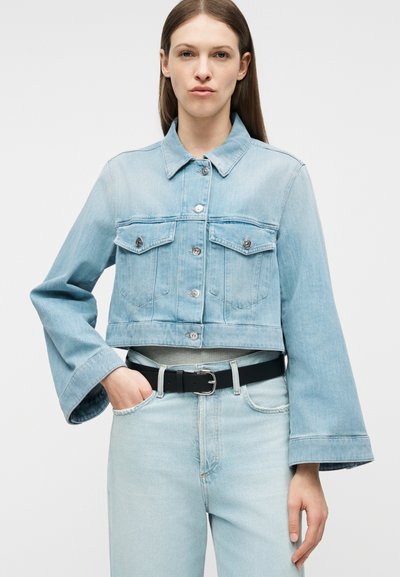 Γυναίκα που φοράει ανοιχτό μπλε τζιν cropped μπουφάν με φαρδιά μανίκια και τζιν παντελόνι ψηλόμεσο με μαύρη ζώνη.