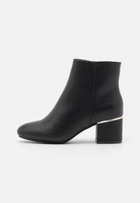 Botas negras hasta el tobillo hechas de cuero liso con punta redonda y un tacón grueso, que presentan un acento metálico en la parte trasera.