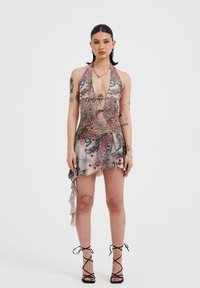 Vestido mini de cuello halter con un estampado colorido de flores y animales, dobladillo con volantes y textura transparente. Combinado con tacones negros de tiras.