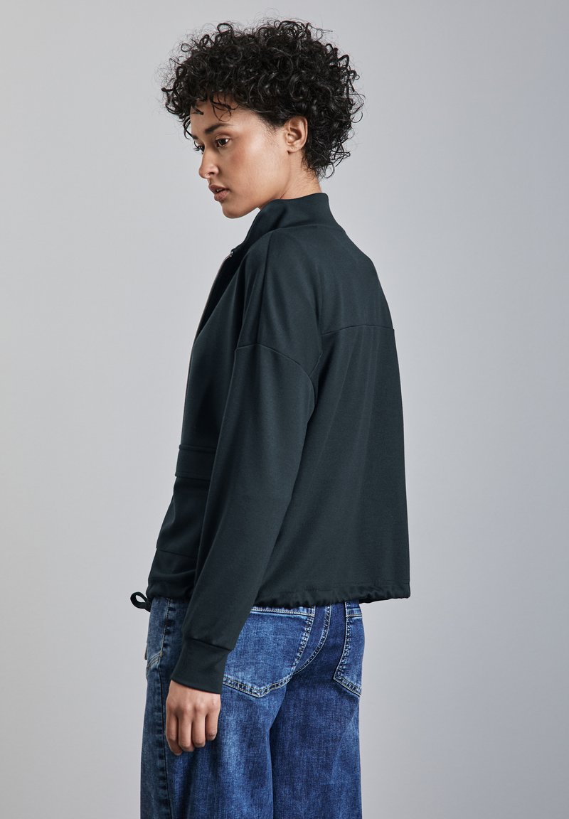 Felpa nera corta con colletto alto e maniche lunghe. Texture morbida, parte anteriore senza dettagli, abbinata a pantaloni di jeans blu con tasche.