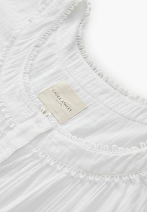White garment with textured fabric, featuring a ruffled neckline, button front, and a label reading "Laura Ashley" for brand identification.