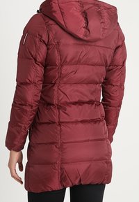 Chaqueta acolchada burdeos con capucha, diseño acolchado y bolsillos laterales, con una textura suave y una parte trasera ligeramente más larga.