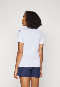 White athletic shirt with short sleeves, featuring a light mesh layer at the hem. Paired with navy shorts. Puma logo on shoulder.