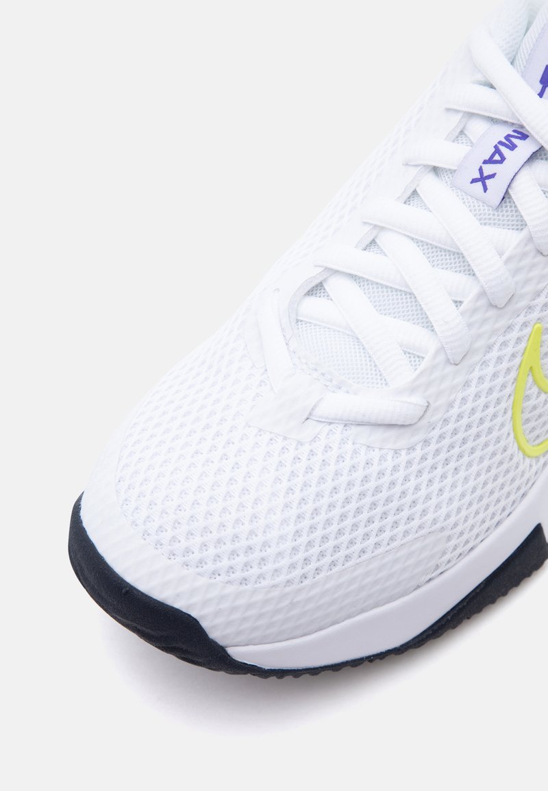 Zbliżenie białego buta sportowego z cholewką z siateczki, białymi sznurówkami, czarną podeszwą i żółtym logo Nike swoosh z boku.