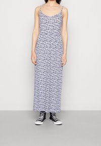 Robe longue à motif floral avec fines bretelles spaghetti, en tissu léger, présentant un schéma de couleurs bleu et blanc et une coupe ample.