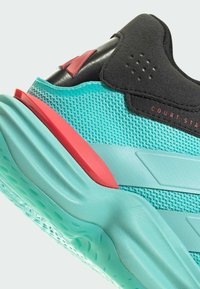 Zapatilla deportiva turquesa con parte superior de malla texturizada, detalles en negro y suela acolchada con un detalle rosa en el talón.