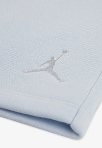 Το ανοιχτό μπλε ύφασμα έχει υφή με έντονο ασημένιο κεντημένο λογότυπο Jumpman. Ομαλές άκρες και λεπτομέρεια διπλωμένης σχεδίασης είναι ορατές.