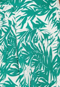 Zelená a bílá látka s tropickým vzorem listů, výrazné tvary a textury vytvářejí živý, vzorovaný design.