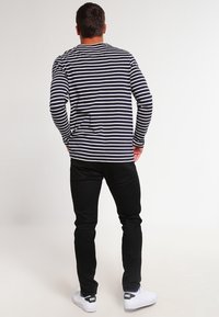 Chemise à rayures bleues et blanches à manches longues associée à un pantalon noir et des baskets blanches, vue de dos. Tissu en coton avec coupe décontractée.