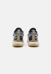 Sportssko med en marineblå og beige fargeskjema, mesh-overdel, polstret krage og gummisåle med teksturerte mønstre og merkevare detaljer.