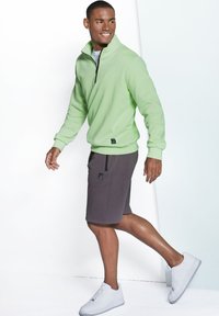 Light green fleece pullover with half-zip and gray shorts, featuring side pockets and a logo patch, paired with white sneakers.