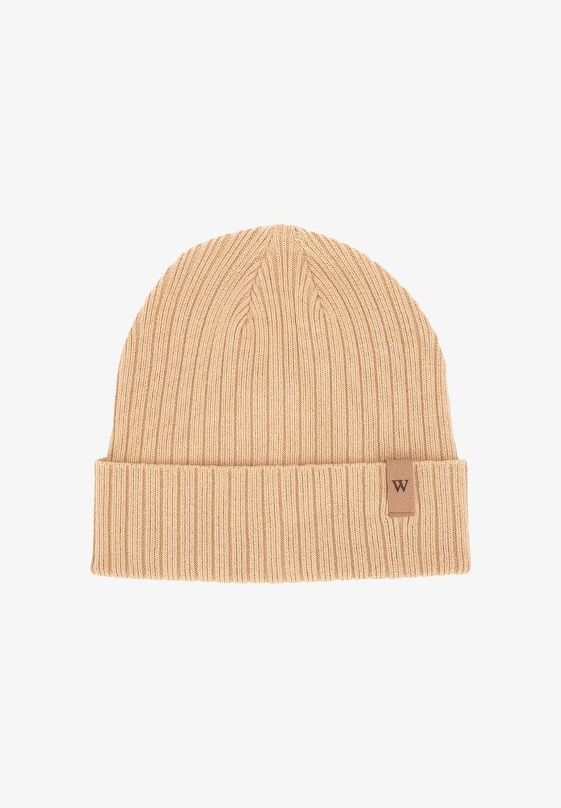 Beige geribbelde gebreide beanie met een opgevouwen boord en een klein bruin leren label met de letter "W". Zacht textuur en warm ontwerp.