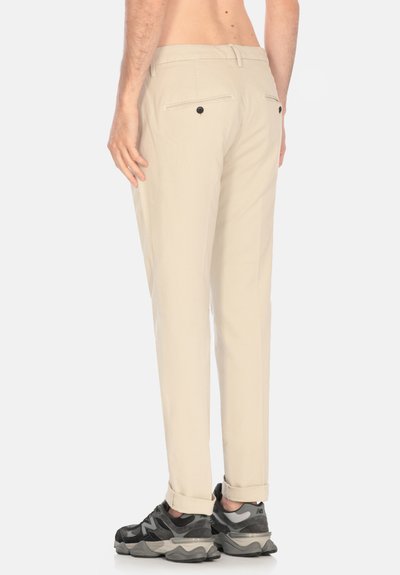Pantaloni beige leggeri con taglio dritto, dotati di due tasche posteriori e risvolti, abbinati a sneakers nere e grigie.