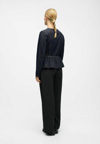 Jeansjacka med peplum i mörkblått och långa ärmar, med en samlad midja. Matchad med svarta vida byxor och svarta skor.