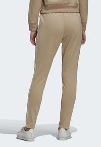 Beige športne hlače v uskem kroju, z belimi stranskimi črtami in rebrastimi manšetami. Gladka tkanina z mehkimi vlakni.