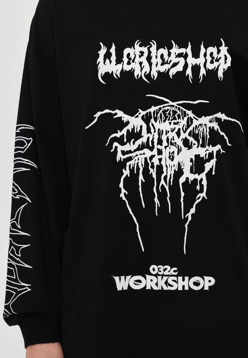 Felpa nera oversize con stampe grafiche bianche, tra cui un logo del brand e disegni intricati su entrambe le maniche.