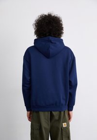 Navy blauwe hoodie met een trekkoordcapuchon, ribbelmanchetten en -zoom, en een ruime pasvorm. Draagt met groene cargo pants, met de achterkant van het kledingstuk zichtbaar.