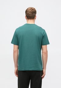 Tyrkysové bavlněné tričko, krátký rukáv, klasický výstřih, má hladkou texturu a rovný lem. Zadní pohled ukazuje minimalistický design bez log.  