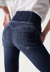 Vaqueros de mezclilla oscuros de cintura alta con una textura suave, que cuentan con dos bolsillos traseros y costuras en contraste a lo largo de las costuras.