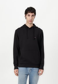 Zwarte hoodie van katoen, met een voorzak en geribde manchetten. Klein logo op de borst. Draag met lichtblauwe jeans.