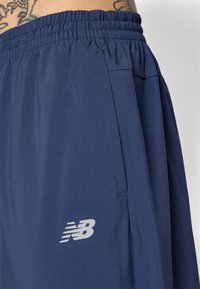 Navy athletic shorts made of lightweight fabric, featuring an elastic waistband and a visible side pocket. Includes a small gray logo detail.