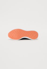 Semelle d'une basket, avec une surface en caoutchouc orange texturé, présentant des motifs arrondis et une bordure blanche sur le bord.