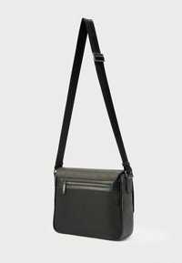 Črna in temno siva torba za prenašanje z nastavljivim naramnim trakom in zadnjim žepom z zadrgo, stoji pokonci na enostavni podlagi.