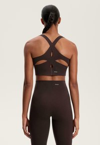 Braun Sport-BH mit einem Kreuzrücken-Design, strukturiertem Stoff, Cut-Out-Details und Logos. Kombiniert mit passenden hochtaillierten Leggings.