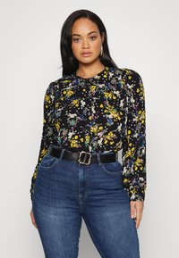 Blusa preta com estampado floral de mangas longas, apresentando uma variedade de flores coloridas e um brilho subtil. Usada com calças de ganga de cintura alta e um cinto preto.