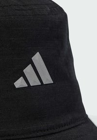 Black bucket hat made of textured fabric features a reflective grey Adidas logo with three stripes on the front.