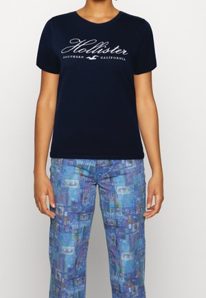 Marineblauwe T-shirt met korte mouwen met witte tekst "Hollister Southern California", gecombineerd met geprinte blauwe broek met abstracte ontwerpen.