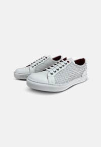 Zapatillas blancas con textura trenzada en los laterales, punta redonda, diseño con cordones y forro de tela roja. Suela de goma con perfil plano.