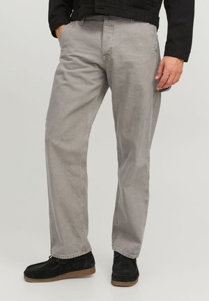 Pantaloni in cotone grigi con vestibilità rilassata, gambe dritta e dettagli di cucitura visibili. Indossati con scarpe in suede nere e una giacca nera.