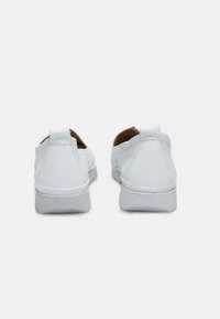 Witte instappers van glad leer met ronde achterkant, minimale stiksels en rubberen zolen. Voorzien van een kleine decoratieve tab aan de hiel.
