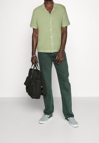 Jasnozielona, teksturowana koszula z krótkim rękawem, ciemnozielone dżinsy, zielono-białe, w kratkę pantofle wsuwane, nosząc czarny plecak.