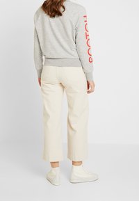 Sudadera gris con texto rojo en la manga, combinada con pantalones anchos color crema y zapatillas altas de color claro. Tejido suave, diseño casual.