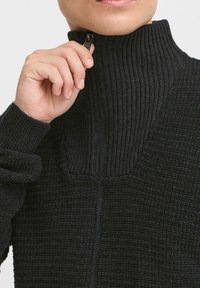 Svart, ribbet zip-up genser med høy krage og teksturert finish. Har en halv-zip design og tettsittende mansjetter.