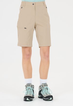 Beige shorts til knæet med lynlåslommer foran og i siden, båret med hvide sokker og grå vandrestøvler med lyseblå snørebånd.