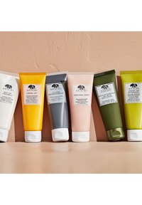 Zes tubes met huidverzorgingsproducten in verschillende kleuren: wit, geel, grijs, roze en groen. Elke tube heeft een etiket met de productnaam en branding.