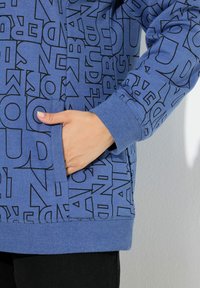 Felpa blu con lettering grafico nero, maniche lunghe, polsini a coste e tasca frontale. Texture liscia con una vestibilità comoda.