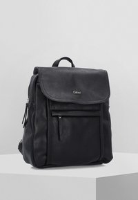 Zaino in pelle nera con finitura testurizzata, chiusura a pattina, tasca frontale con zip e tasche laterali doppie; design minimalista con manico superiore.