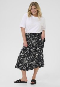 Fustă neagră cu flori, cu tiv volan, asociată cu un tricou alb cu mânecă scurtă și sandale negre de tip slide. Fusta are un brâu strâns.