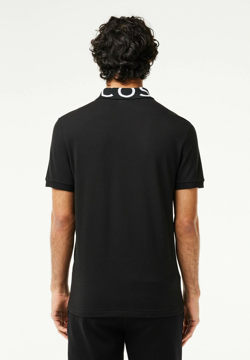 Schwarzes Poloshirt mit geripptem Kragen und kontrastierendem Schriftzug. Kurze Ärmel und eine glatte, weiche Textur. Enganliegende Passform, minimalistisches Design.